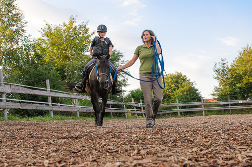 Kind reitet unter professioneller Begleitung auf Pony in der Manege von Reiterhof von Theresia Burger in Waltenhofen-Herzmans am Niedersonthofener See im Oberallgäu